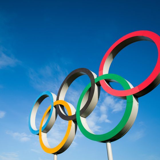 Olympic rings sculpture with five interlinked rings in blue, yellow, black, green, and red against a blue sky with some clouds.