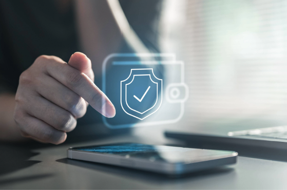 A person touches a transparent security shield icon with a check mark that appears above a smartphone, symbolising digital security or protection.