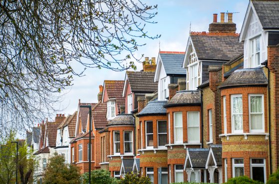Series of traditional brick terraced houses with pitched roofs, bay windows and small front gardens, under a partly cloudy sky.