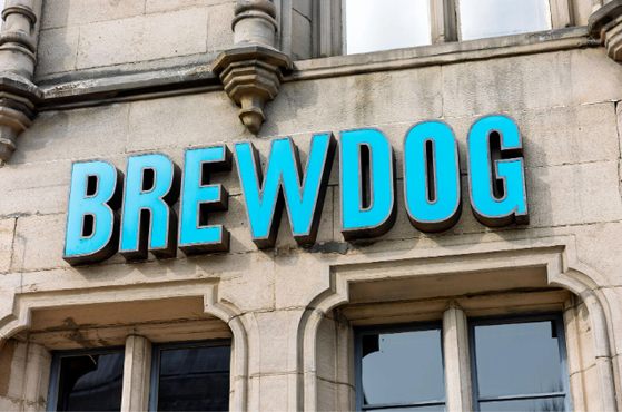 Stone building facade with a bright blue BREWDOG sign in bold lettering above arched windows, framed by decorative stonework and columns.