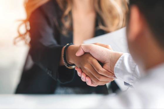 Close-up of a woman and man shaking hands in a professional setting, with sunlight in the background.