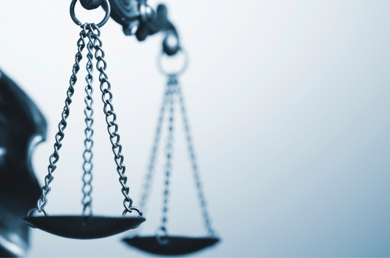 Close-up of a metal balance scale with hanging chains, symbolising justice, set against a soft blue gradient background.