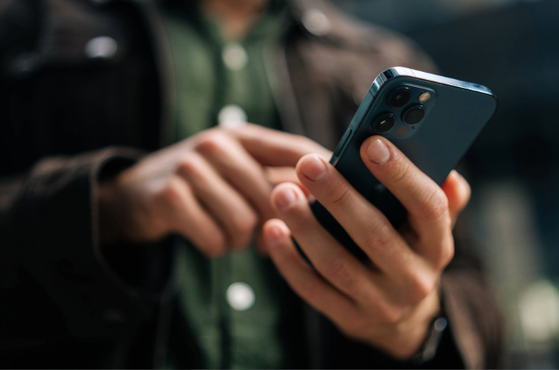 Person in a dark jacket and green shirt using a blue smartphone outdoors.