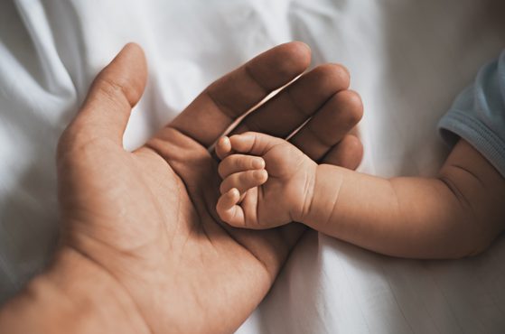 Close-up small hands of baby is lying in men of his father hands, concept of caring, fatherhood, family