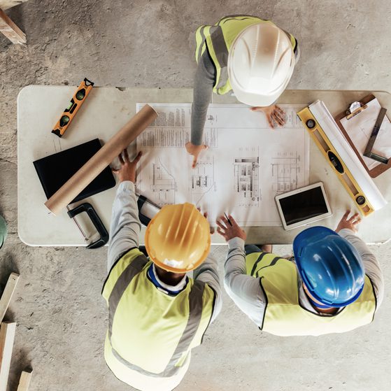 Construction workers standing over blueprints arial shot