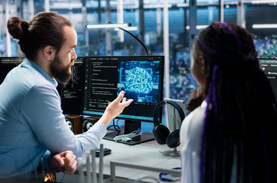 Two scientists in a high-tech lab discuss a digital brain diagram on a monitor, surrounded by computer screens, equipment, and a cityscape through the window.