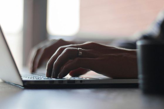 Close-up of hands typing on a laptop keyboard with a blurred background.