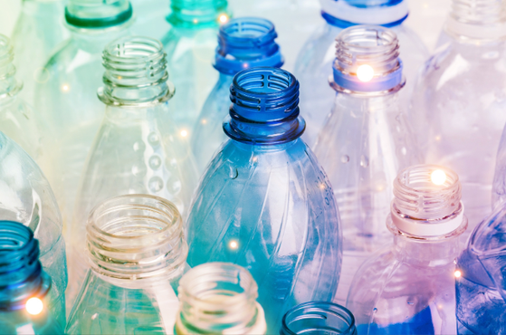 Close-up of many translucent plastic bottles in blue, teal and purple hues, empty with threaded necks, light reflections and soft out-of-focus highlights scattered throughout.
