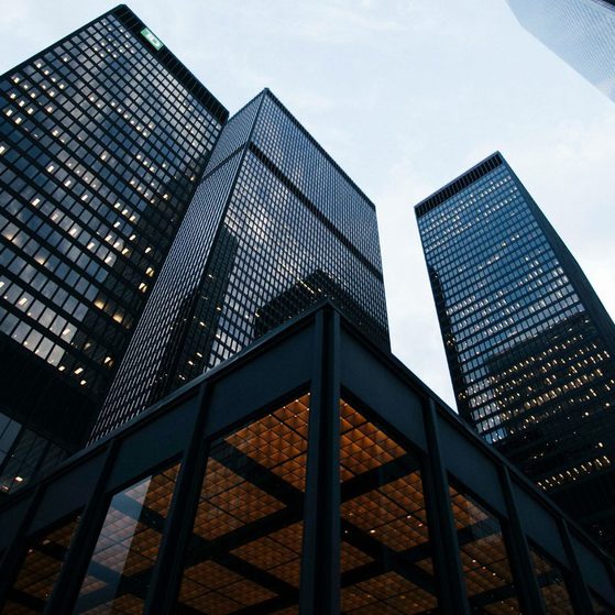 Several tall modern glass skyscrapers viewed from below, with reflections on their surfaces and a partly cloudy sky in the background.