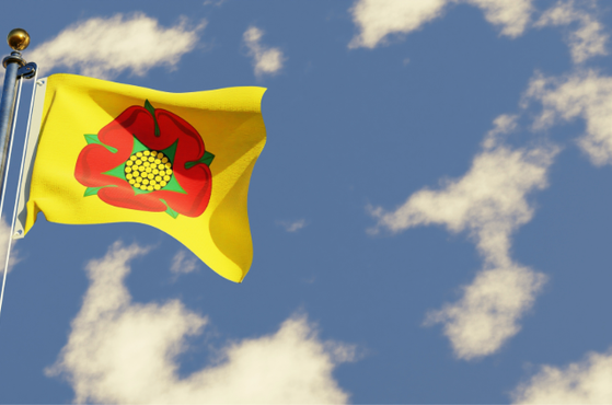 Yellow flag with a red poppy emblem flutters on a tall flagpole against a bright blue sky dotted with white clouds, capturing a crisp, windy day scene.