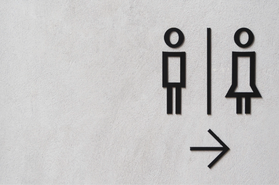 Two minimalist black restroom icons for male and female separated by a vertical divider, with a right-pointing arrow beneath on a light textured wall.