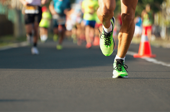 Close-up of a runner's neon green shoes as they race down a city street, with blurred competitors and an orange traffic cone in the background.