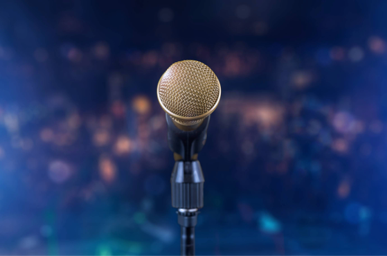 Close-up of a gold mesh microphone on a stand on a concert stage with a soft blue bokeh backdrop and twinkling lights.