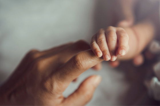 A baby's hand gently gripping an adult's finger, focusing on the hands with a soft, blurred background.
