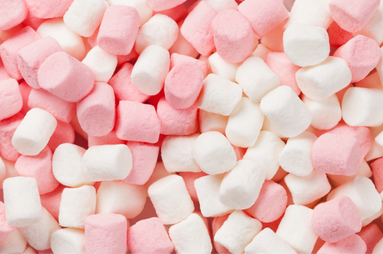 Dense jumble of pink and white mini marshmallows, small fluffy cylinders filling the frame with pastel confectionery.