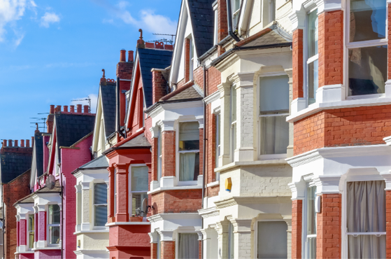 Row of colourful Victorian terraced houses with ornate white trim, bay windows and decorative brickwork under a bright blue sky.