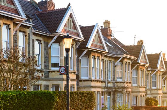 Row of Victorian-style terraced houses with bay windows, pitched roofs, and decorative trim, illuminated by warm sunlight.