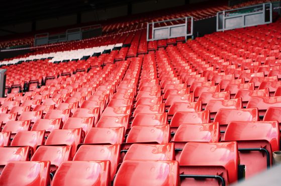 Numerous red stadium seats arranged in rows, with some empty spaces and a few sections with white seats in the background.