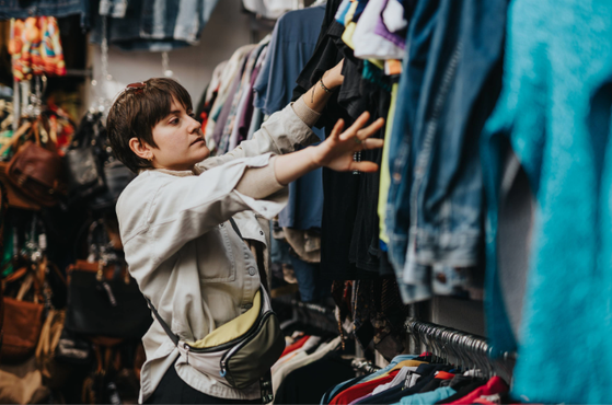 A young woman shopping for clothes, browsing a rack of colourful garments in a store.