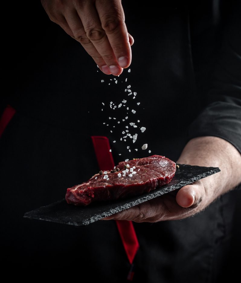 Chef sprinkling salt onto a steak