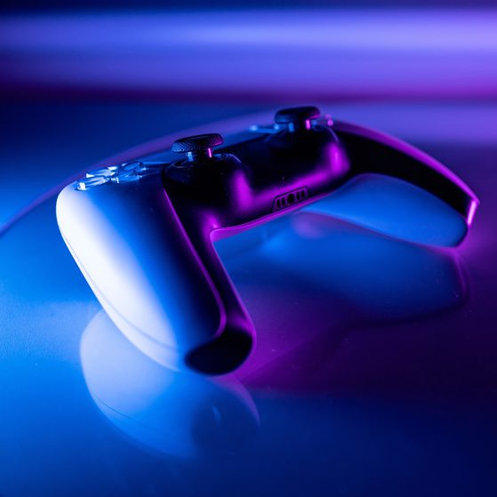 A gaming controller resting on a reflective surface with colourful purple and blue lighting, creating a vibrant, futuristic atmosphere.