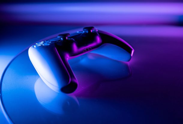 A gaming controller resting on a reflective surface with colourful purple and blue lighting, creating a vibrant, futuristic atmosphere.