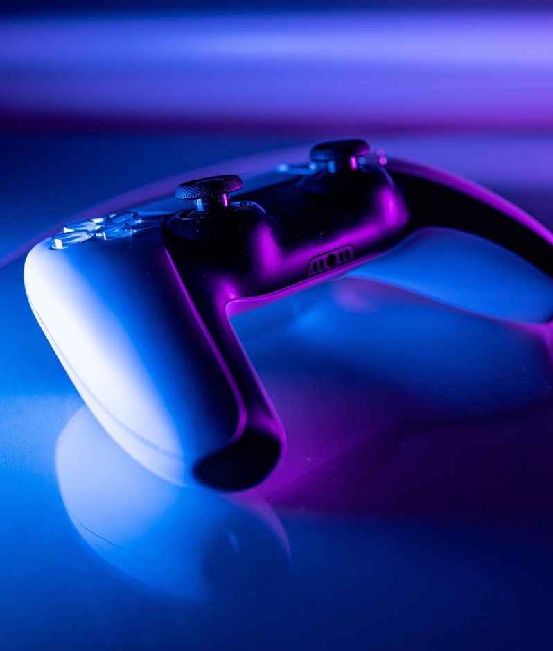 A gaming controller resting on a reflective surface with colourful purple and blue lighting, creating a vibrant, futuristic atmosphere.