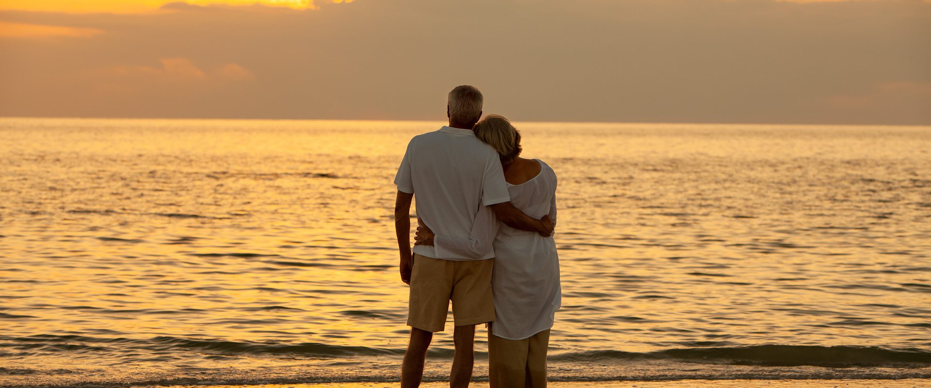 Couple embracing on beach and looking out to the sea at sunset