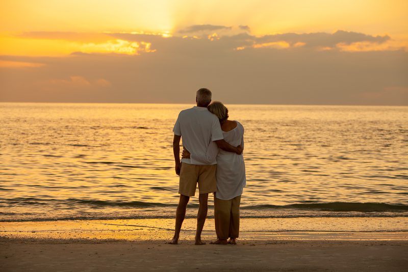 Couple embracing on beach and looking out to the sea at sunset